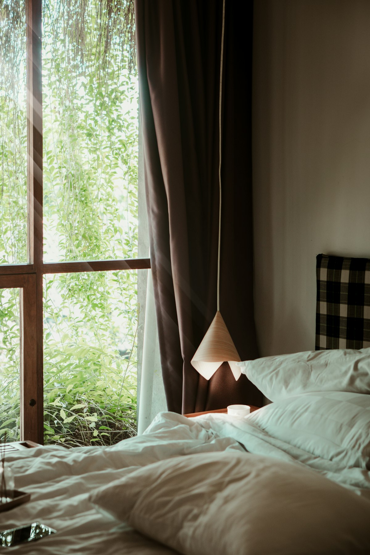 Hotel bed with white linen beside a garden window