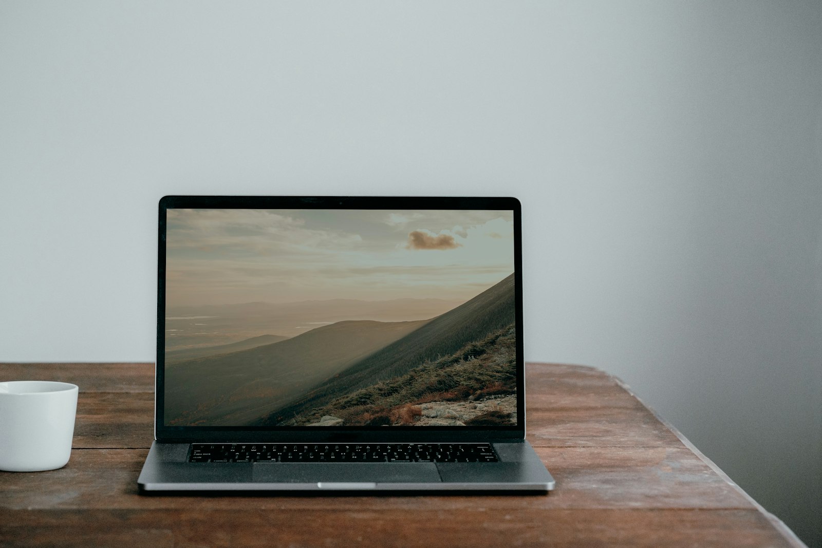 Laptop on a wooden table beside a white ceramic cup